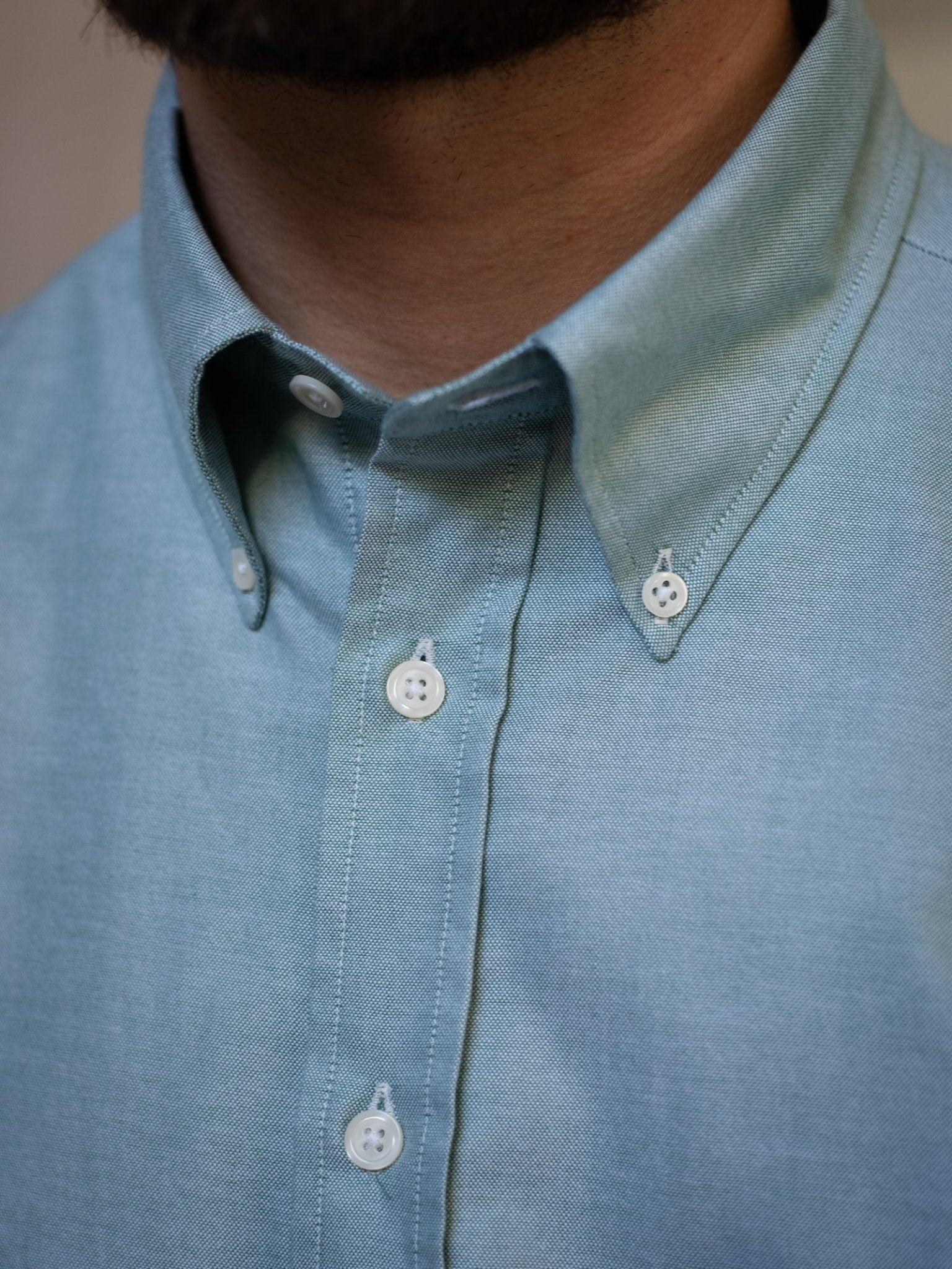 Close-up of a person wearing the Campbell's of Beauly Oxford Button Down Shirt in light blue, featuring a neatly buttoned collar and white buttons, with part of their beard and neck visible.