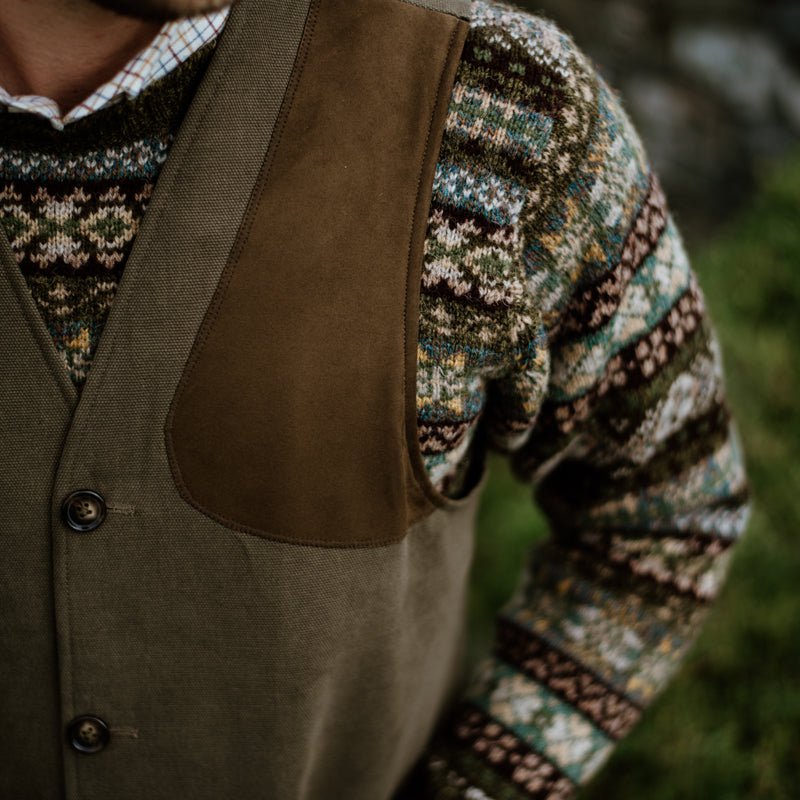 Close-up of a person wearing Campbells of Beauly Cotton Shooting Waistcoat over a colorful knit sweater with green, blue, brown, and white patterns; only the torso and part of an arm are visible—ideal for countryside pursuits.