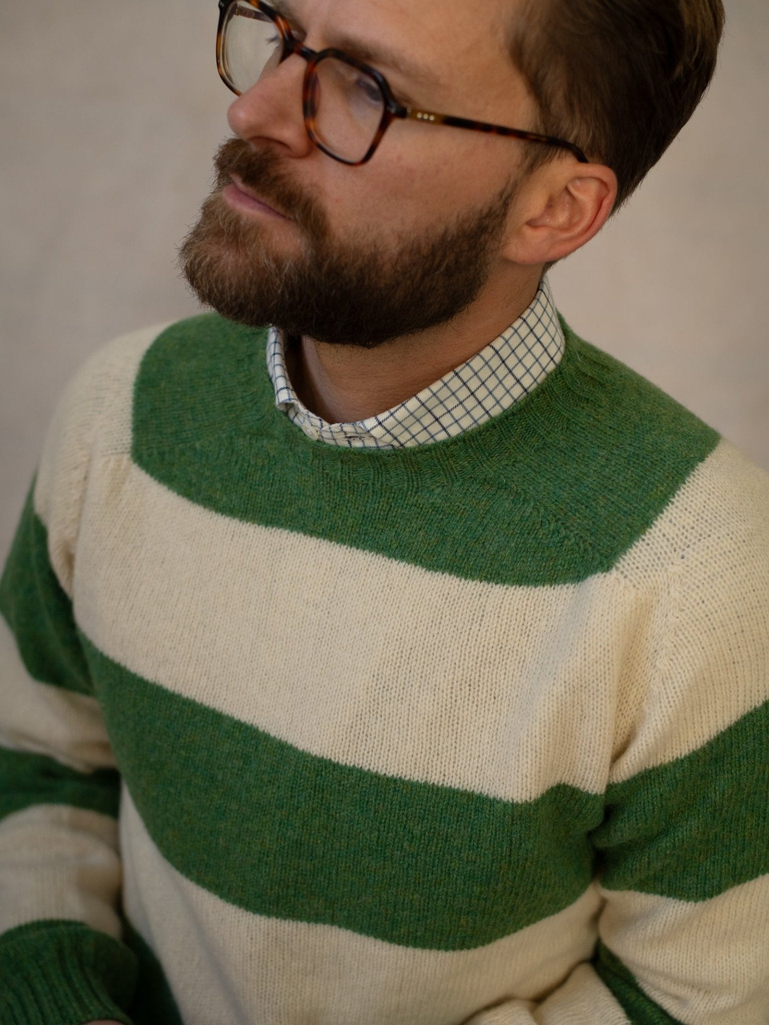 A man with a beard and glasses wears the Campbell's of Beauly Shetland Stripe Crew Jumper over a checkered shirt, looking slightly upward with a neutral expression.