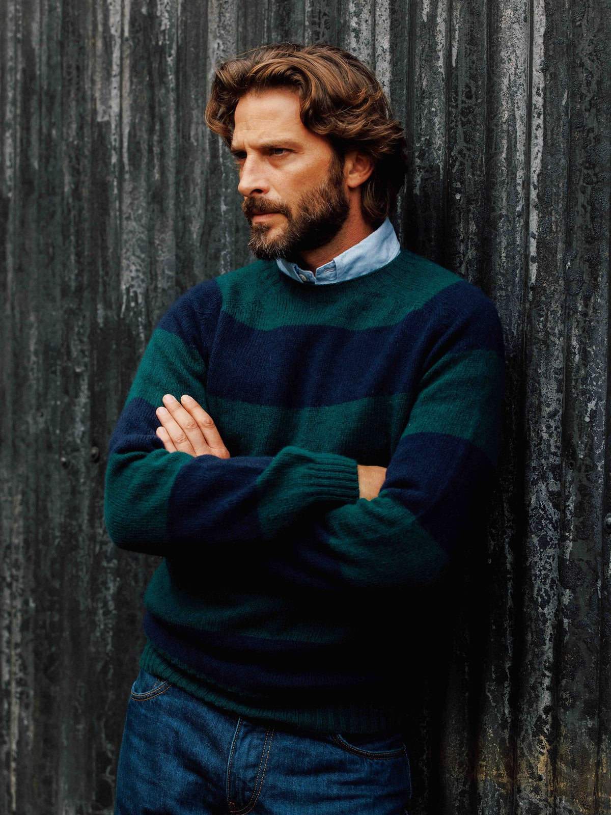 A bearded man stands with his arms crossed, wearing a dark green and navy blue Campbell’s of Beauly Shetland Stripe Crew Jumper over a light blue collared shirt.