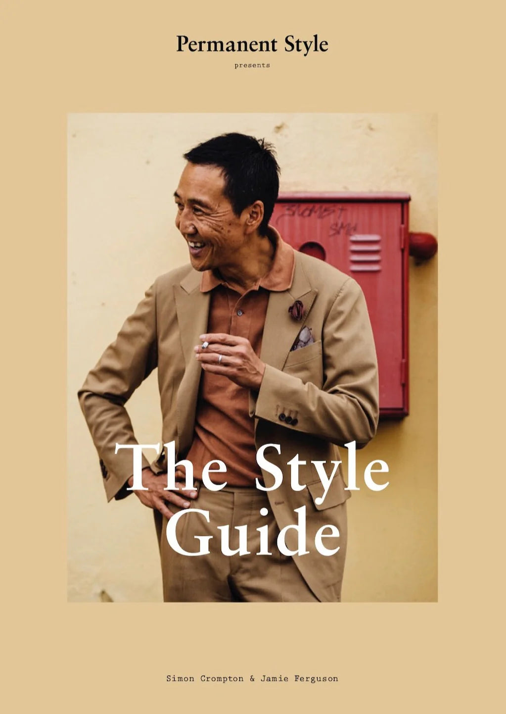 A man in a tan suit and rust polo stands by a beige wall with a red mailbox. Text: “The Style Guide by Permanent Style – menswear insights from Simon Crompton & Jamie Ferguson.”.
