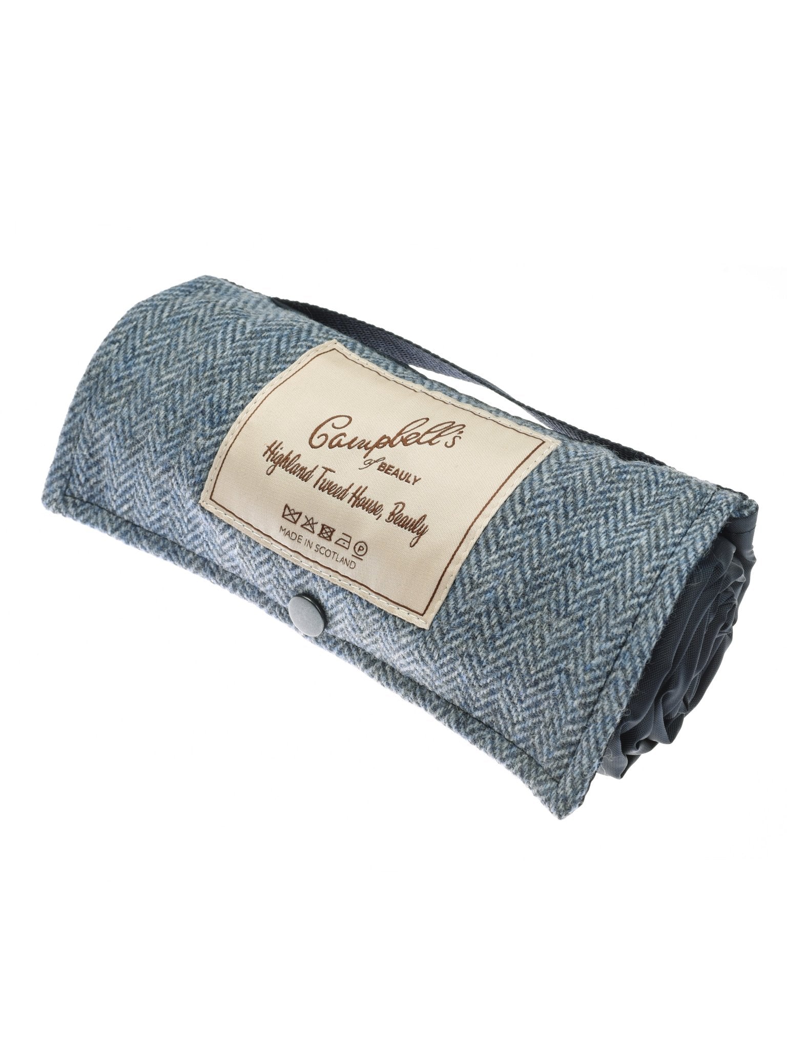 The Walker Camper Picnic Rug by Campbells of Beauly is a rolled-up blue travel blanket made from British wool with a button closure and label, ideal as a picnic rug for outdoor adventures.