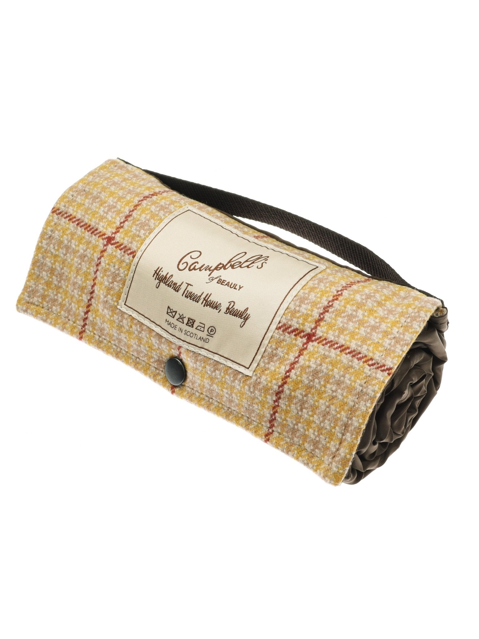 The Walker Camper Picnic Rug by Campbells of Beauly features a gold plaid pattern, crafted from British wool and secured with a black strap and button. The label reads “Campbell’s of Beauly, Highland Tweed House Family.”.